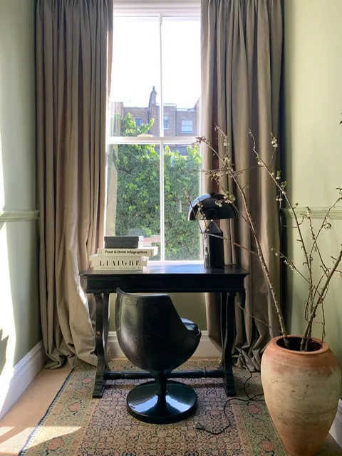 Long taupe curtains resting on the floor either side of a sash window in a home study